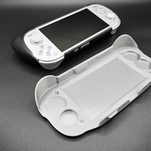 以下が含まれることがあります： 黒い画面と白いボタンが付いた携帯型ゲーム機と、明るい灰色の保護ケース。コンソールは黒とシルバーのデザインです。ケースはコンソールに合うように設計されており、ボタンとコントロール用の開口部があります。