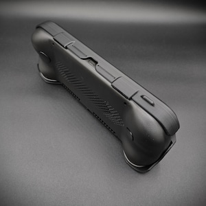 May include: A black handheld gaming device with a textured surface and multiple buttons. The device has a curved design with ergonomic grips on each side. The top edge features additional buttons and a USB-C port.