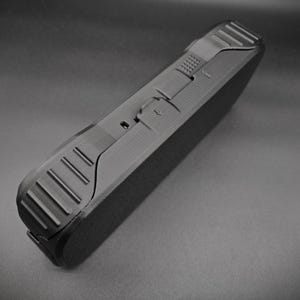 May include: A black rectangular case with textured sides and a matte finish. The case has a hinged design with a latch and a series of parallel grooves on the edge. The overall design is sleek and modern.