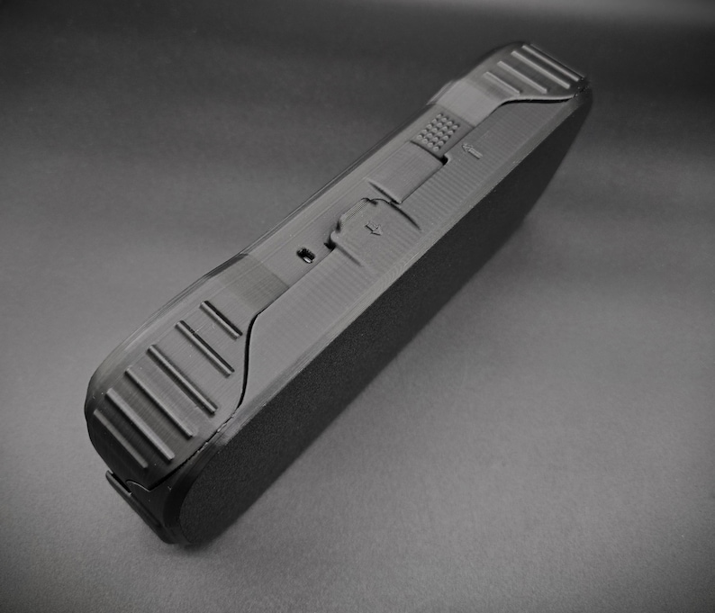 May include: A black rectangular case with textured sides and a matte finish. The case has a hinged design with a latch and a series of parallel grooves on the edge. The overall design is sleek and modern.