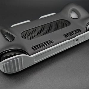 May include: A black and gray handheld gaming console case. The case has a textured black body with gray accents, including the grips and edges. It features a mesh vent and several button placements, designed for a comfortable grip and optimal gaming experience.