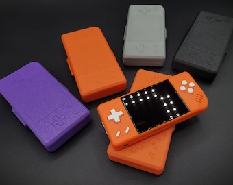 May include: Five handheld game consoles in various colours, including orange, purple, grey, and black. The consoles have a screen, buttons, and a plus sign on the front.