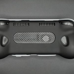 May include: Black handheld gaming device with a white trim. The device features a central speaker grill, two ventilation slots, and gray buttons. The ergonomic design includes rounded grips and a sleek, modern aesthetic.