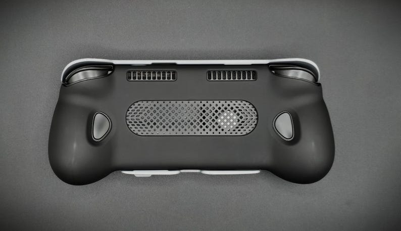 May include: Black handheld gaming device with a white trim. The device features a central speaker grill, two ventilation slots, and gray buttons. The ergonomic design includes rounded grips and a sleek, modern aesthetic.