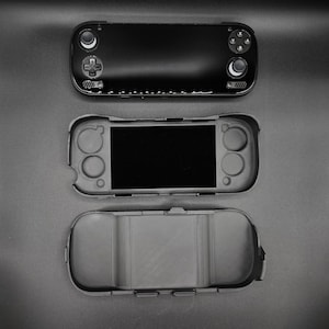 May include: Black handheld gaming console with a protective case, and a separate bottom case. The console features a screen, buttons, and control sticks. The protective case is gray and fits the console's shape.