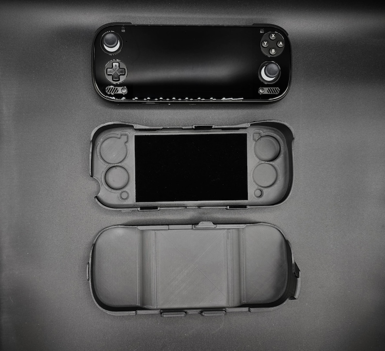 May include: Black handheld gaming console with a protective case, and a separate bottom case. The console features a screen, buttons, and control sticks. The protective case is gray and fits the console's shape.