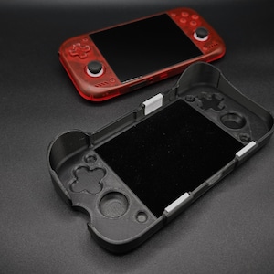 May include: A handheld gaming console with a translucent red plastic shell and black screen, positioned above a black 3D-printed protective case featuring cutouts for buttons, joysticks, and the screen, with small white accent tabs along the edges.