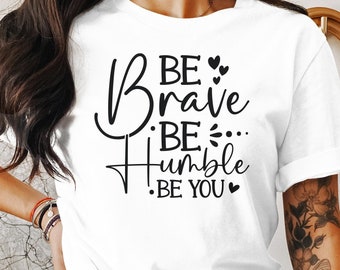 Op de afbeelding: Wit T-shirt met zwarte tekst die "Be Brave Be Humble Be You" met kleine hartjes zegt.