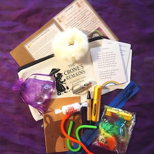 May include: A selection of calming items, including a canvas bag with text, a fluffy scrunchie, a purple pouch with clear stones, and cards with rainbow prompts. Also includes a small perfume bottle and a Love Hearts sweet.