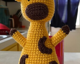 May include: A crocheted giraffe toy with brown spots. The giraffe is yellow and has a brown nose and black eyes.