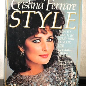 May include: A book titled "Cristina Ferrare STYLE" with a subtitle "HOW TO HAVE IT IN EVERY PART OF YOUR LIFE" by Cristina Ferrare DeLorean & Sherry Suib Cohen. The cover features a woman with dark hair and a sparkly silver top.