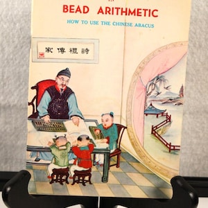 May include: A vintage book cover with a colorful illustration of a teacher and three students learning bead arithmetic using an abacus. The book title is "The Fundamental Operations in Bead Arithmetic: How to Use the Chinese Abacus".