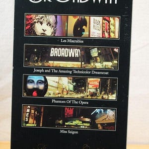 May include: A black CD case titled "The Best of Today's Broadway" featuring images from "Les Miserables," "Joseph and the Amazing Technicolor Dreamcoat," "Phantom of the Opera," and "Miss Saigon." The case is displayed on a black stand.