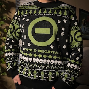 May include: Black and green Christmas sweater with a green circle and a white bar across the center. The text "Type O Negative" is printed below the circle. The sweater has a pattern of skulls, snowflakes, and Christmas trees.