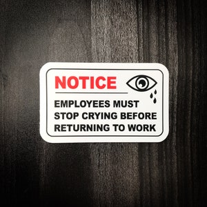 May include: A white sticker with a black border and the word "NOTICE" in red. Below, it reads "EMPLOYEES MUST STOP CRYING BEFORE RETURNING TO WORK." An eye with tear drops is on the right.