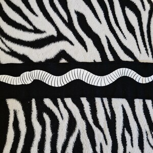 May include: A black fabric patch with a white, segmented worm design. The patch is on a black and white zebra print background.