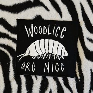May include: Black iron-on patch with white text and a white illustration of a woodlouse. The text reads "Woodlice are nice."