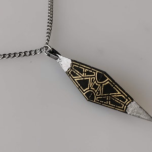 May include: A silver chain necklace with a black and gold pendant. The pendant is shaped like a diamond and has a geometric design.