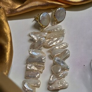 May include: A pair of gold earrings with a large, round, white pearl at the top and a long, dangling chain of smaller, irregular white pearls.