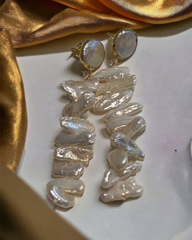 May include: A pair of gold earrings with a large, round, white pearl at the top and a long, dangling chain of smaller, irregular white pearls.