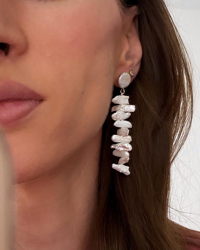 May include: A pair of long, silver earrings with a cluster of white baroque pearls hanging from a small silver disc.