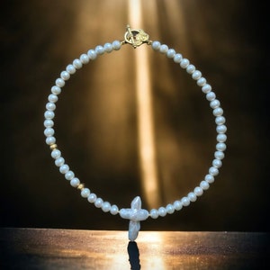 Op de afbeelding: Een witte parelketting met een gouden sluiting en een parel kruis hanger.
