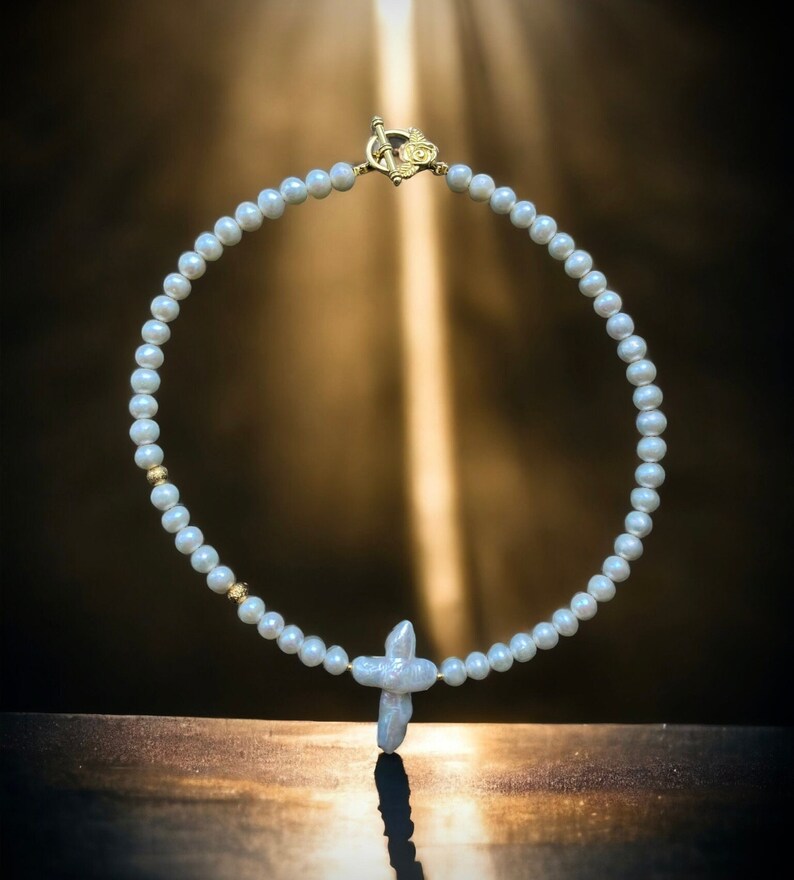 Op de afbeelding: Een witte parelketting met een gouden sluiting en een parel kruis hanger.