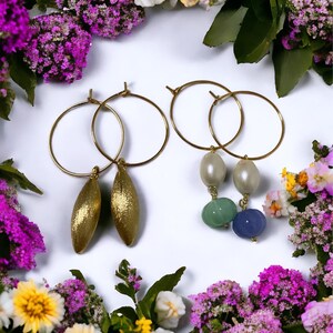 May include: A pair of gold hoop earrings with two different charms. One charm is a pair of gold teardrop shapes and the other charm is a pair of white and green beads.