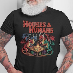 Puede incluir: Camiseta negra con el texto "HOUSES & HUMANS" y una ilustración de fantasía. El gráfico muestra cuatro dragones, rojos, azules y verdes, reunidos alrededor de una mesa con un tablero de juego. Los dragones tienen alas detalladas.