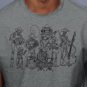 Puede incluir: Una camiseta gris con un dibujo lineal negro de una banda de músicos robot tocando varios instrumentos, incluyendo un acordeón, una tuba, una batería, una guitarra y un contrabajo. Los miembros de la banda llevan sombreros de vaquero. La persona que lleva la camiseta está sonriendo.