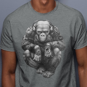 May include: A heather grey t-shirt featuring a black and white illustration of a monkey wearing headphones and tattoos. The monkey is sitting with its legs crossed and has a serious expression on its face.