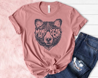 May include: A dusty rose t-shirt with a graphic of a bear wearing heart-shaped sunglasses that say "Mama Bear" in navy blue.