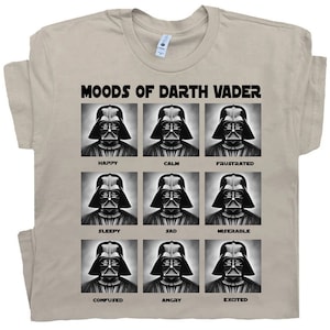 Könnte beinhalten: Ein beiges T-Shirt mit einer Grafik von Darth Vaders Gesicht in neun verschiedenen Stimmungen. Die Stimmungen sind mit "Happy", "Calm", "Frustrated", "Sleepy", "Sad", "Miserable", "Confused", "Angry" und "Excited" beschriftet.