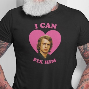 May include: Black t-shirt with a pink heart graphic featuring a portrait and the text "I CAN FIX HIM". The shirt is made of a soft material and is suitable for casual wear.