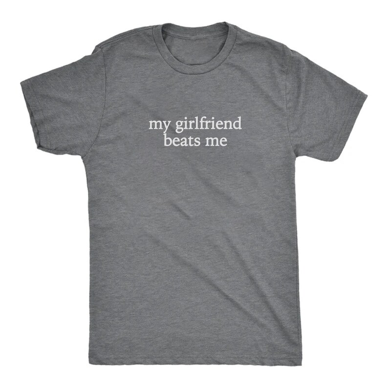 May include: A heather gray t-shirt with the text "my girlfriend beats me" in white, centered on the chest. The shirt has short sleeves and a crew neck.