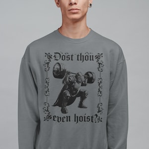 Op de afbeelding: Grijze sweatshirt met een zwarte afbeelding van een middeleeuwse ridder die een halter optilt. De tekst "Dost thou even hoist?" is boven en onder de ridderillustratie in een decoratief lettertype gedrukt. Ronde hals.