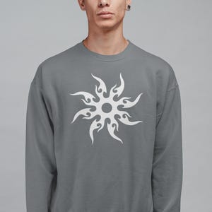 Puede incluir: Una sudadera gris con un dise&ntilde;o de sol blanco. La sudadera de cuello redondo es de color liso y tiene mangas largas. El dise&ntilde;o del sol est&aacute; centrado en la parte delantera de la sudadera.