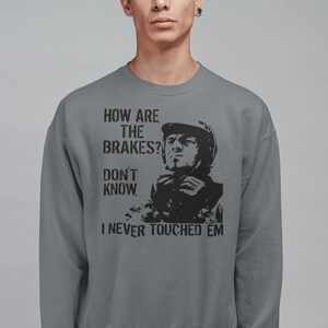 May include: A grey sweatshirt with a black graphic print of a man in a racing helmet. The text on the sweatshirt reads "How are the brakes? Don't know, I never touched 'em."