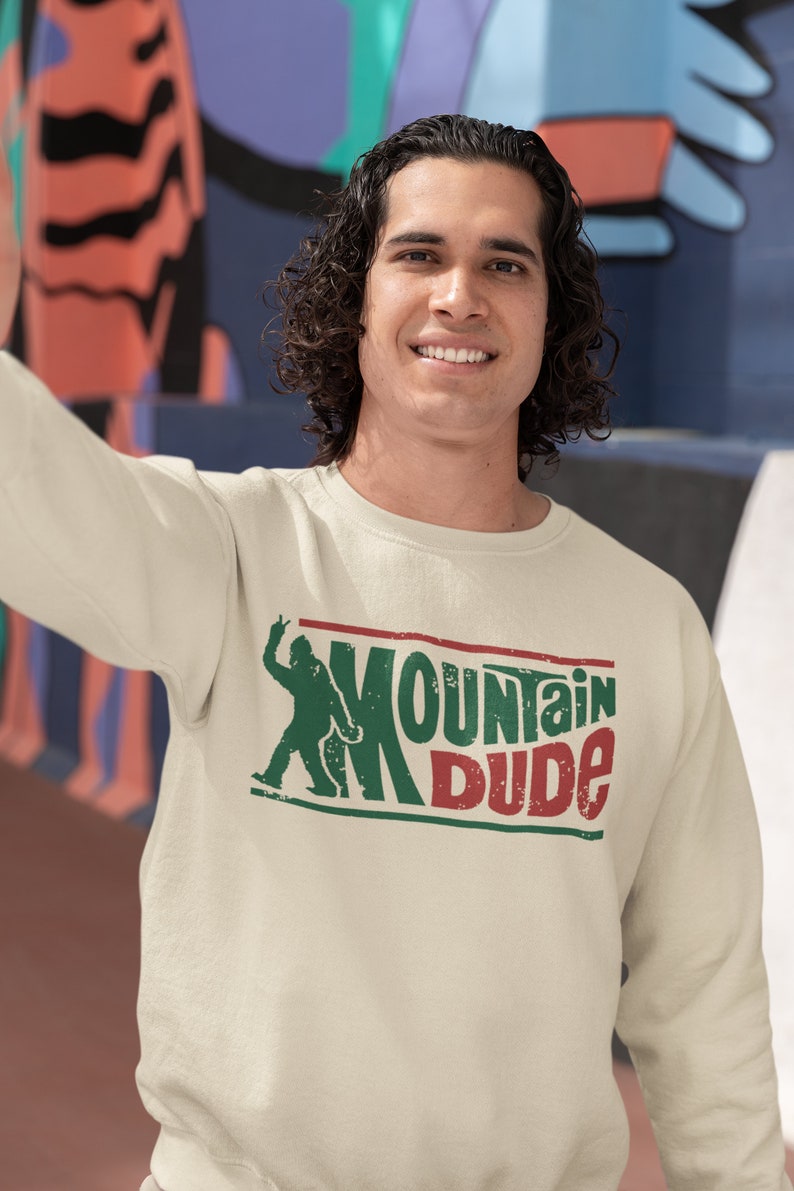 May include: A cream-colored sweatshirt with a green and red graphic of a person with the text "Mountain Dude".