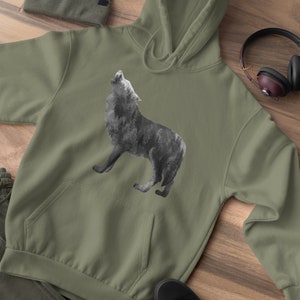 May include: A green hooded sweatshirt with a black and white wolf howling graphic print. The sweatshirt is laid out on a wooden surface with a beanie, headphones, and shoes.