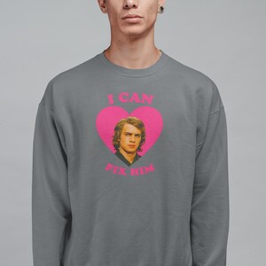 May include: Gray sweatshirt with a pink heart graphic featuring a portrait of a man and the text "I CAN FIX HIM" in pink. The sweatshirt is a crew neck style.