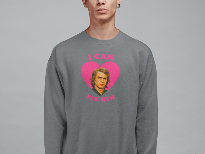 May include: Gray sweatshirt with a pink heart graphic featuring a portrait of a man and the text "I CAN FIX HIM" in pink. The sweatshirt is a crew neck style.