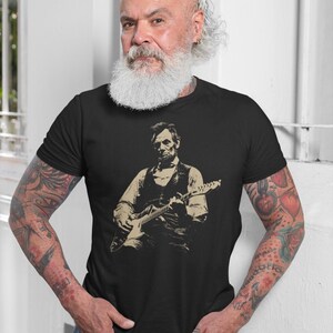 Peut inclure: T-shirt noir avec une image s&eacute;pia d'Abraham Lincoln jouant de la guitare. L'image montre Lincoln en gilet et chemise, tenant la guitare. La personne portant le t-shirt a des tatouages sur les bras.