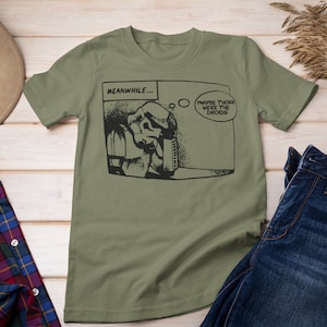 May include: A green t-shirt with a black and white comic strip graphic. The comic strip features a character with a thought bubble that says "Maybe those were the droids". The text "MEANWHILE..." is above the comic strip.