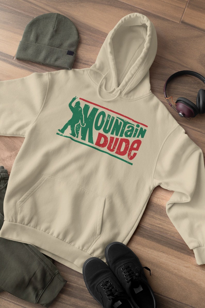 May include: A beige hoodie with a green and red graphic that says "Mountain Dude" and a silhouette of a person with their arms raised.