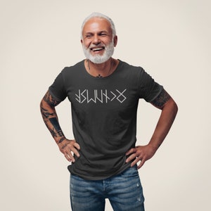 May include: A dark gray t-shirt with a white graphic design of a symbol. The symbol is made up of lines and arrows. The person wearing the shirt is smiling.