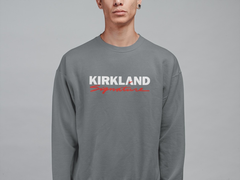Puede incluir: Sudadera gris de cuello redondo con el texto "KIRKLAND Signature" en blanco y rojo. La sudadera es de color liso y tiene un dise&ntilde;o sencillo y cl&aacute;sico.