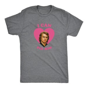 May include: A heather gray t-shirt featuring a pink heart with the image of a man inside. The text "I CAN FIX HIM" is printed above and below the heart in pink. The shirt is a crew neck style.