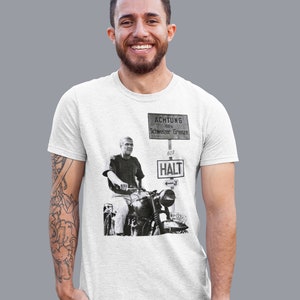 May include: White t-shirt with a black and white image of a man riding a motorcycle. The image includes a sign that reads "ACHTUNG 100 m Schweizer Grenze 607 HALT".