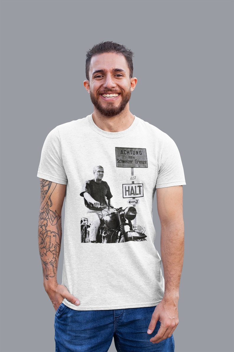 May include: White t-shirt with a black and white image of a man riding a motorcycle. The image includes a sign that reads "ACHTUNG 100 m Schweizer Grenze 607 HALT".